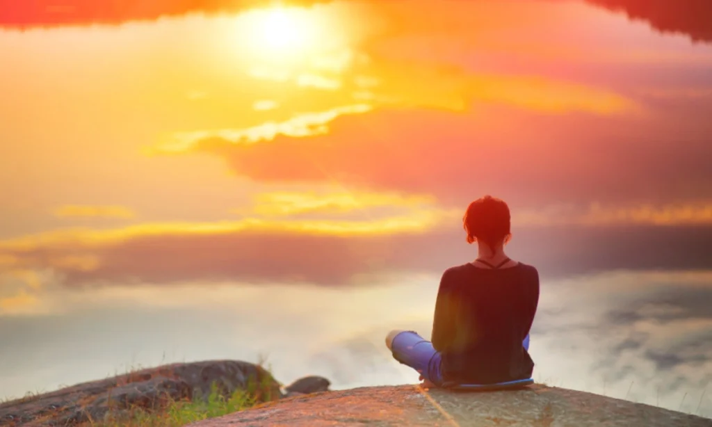 Mujer medita en loto, alto con vista al lago, buscando armonía mental | Qué Onda