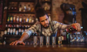 Tequila de Lujo: un Bartender profesional sirve cuidadosamente un destilado premium en una hilera de vasos tipo Shot | Qué Onda
