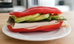 Sándwich de Morrón relleno de pavo y aguacate sobre un plato blanco | Qué onda