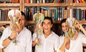 Villalobos Brothers posando con violines decorados con arte colorido frente a una biblioteca | Qué onda